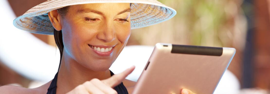 woman relaxing by the pool wearing a straw hat playing at Jackpot Capital on her tablet