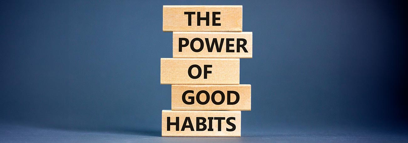 5 wooden blocks stacked on top of each other with "The Power Of Good Habits" written one word on each block.