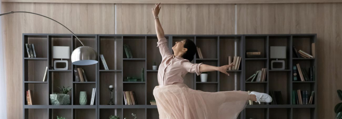a woman in a flowing whitish dress dancing ballet in her living room
