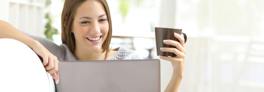 woman casually playing at Jackpot Capital on her laptop on her sofa with a cup of coffee