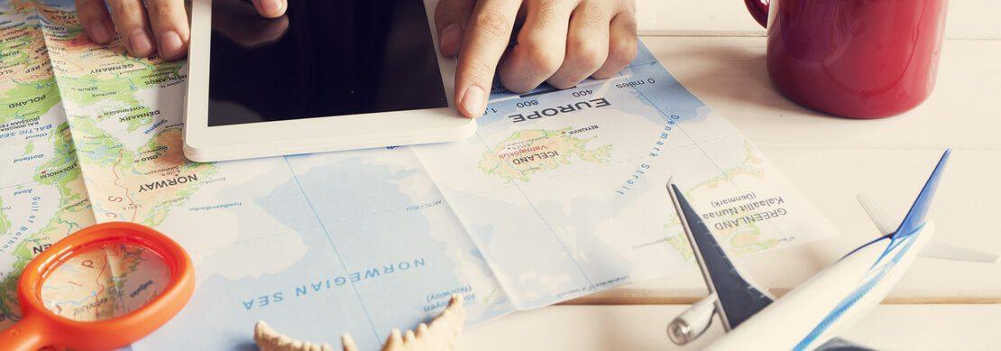 person planning a trip with a map, camera, plane model, shell on the table