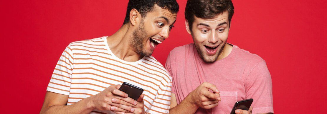 two guys having fun playing at Jackpot Capital on their phones on a red background