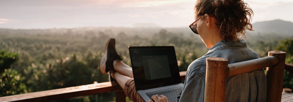 woman working on her laptop sitting on the porch looking out over beautiful forest view