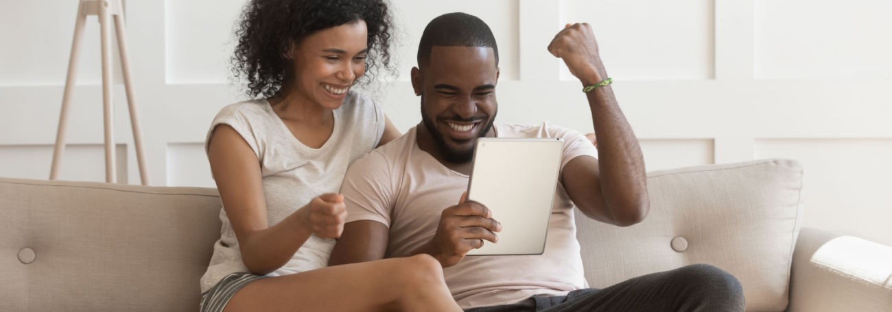 a young couple comfortably sitting on their sofa enjoying playing casino games on their tablet