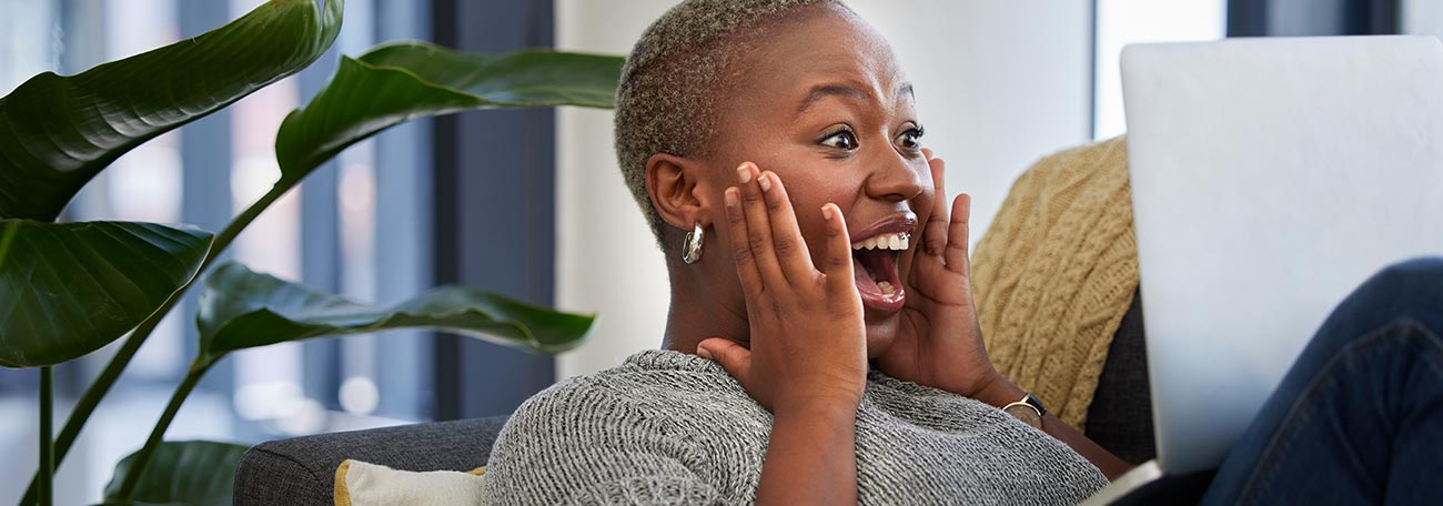 a thirty-something black woman with very short hair enjoying online casino gaming on her laptop while comfortably on her sofa