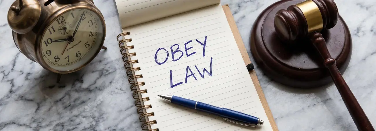 obey the law written on a note pad with a gavel, pen, and clock beside it