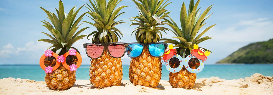 four pineapples ona Caribbean beach wearing pink or blue sunglasses