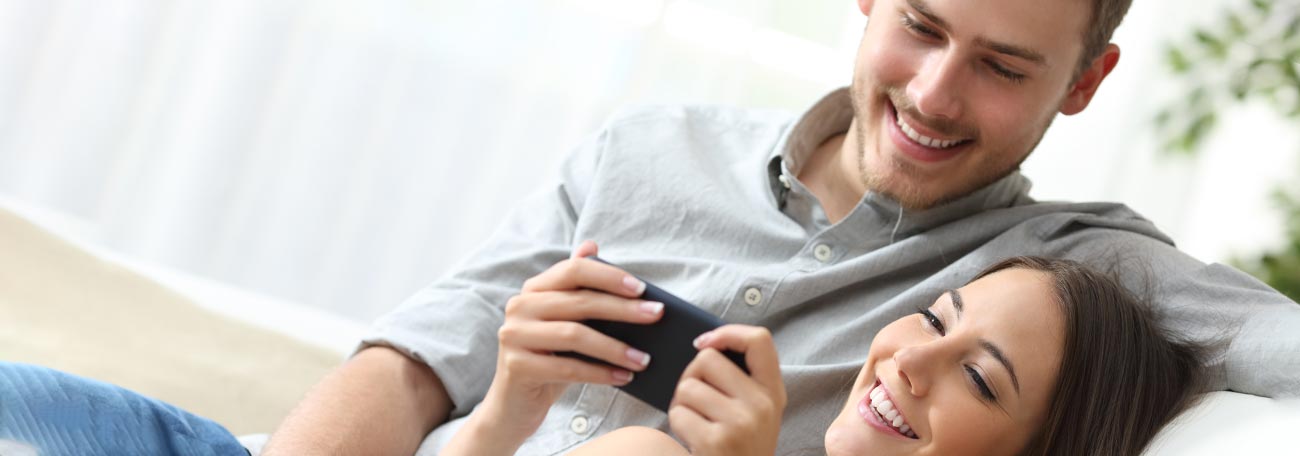 a young couple showing romantic side of gaming on mobile as they are curled up on a sofa together