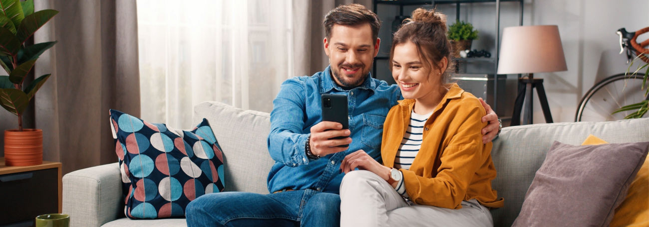 young couple enjoying online casino gaming on their sofa. The man has his arm around the woman.