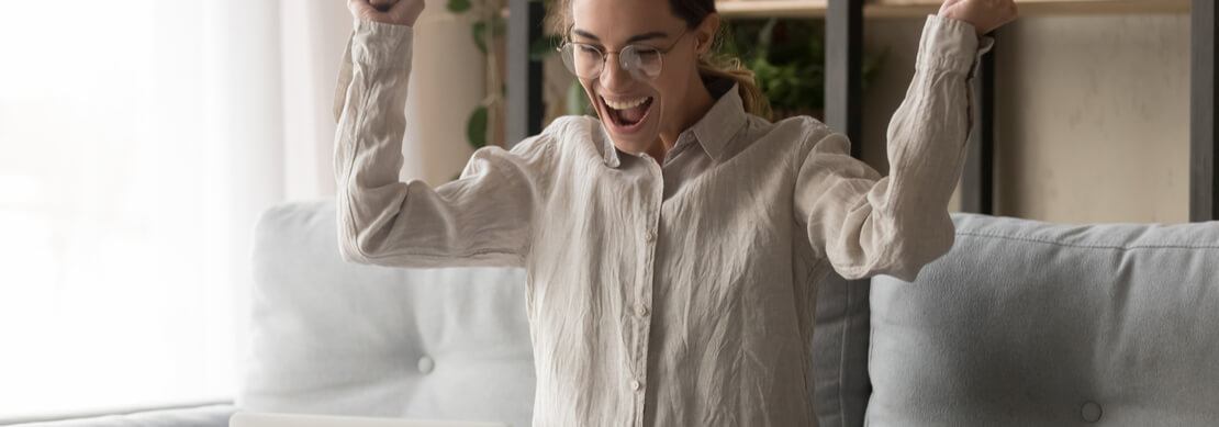 ecstatic joy as a millennial woman sitting on her sofa at home reacts to winning a progressive jackpot