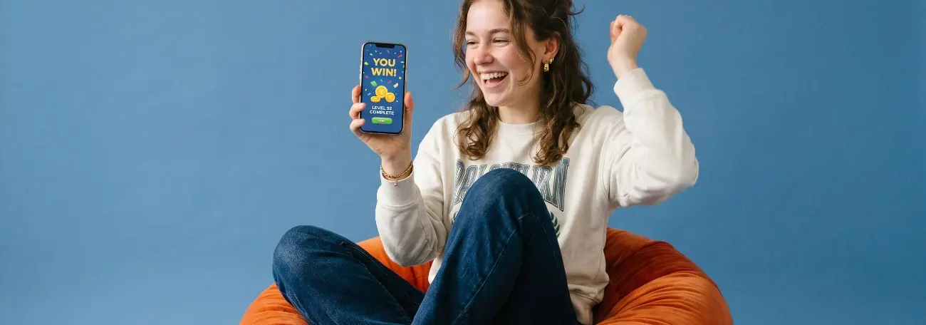 young woman sitting on a puff chair celebrating a win on her phone