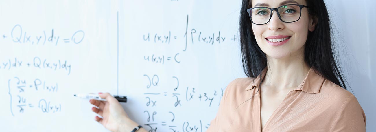 attractive woman mathematician with glasses and dark hair at the whiteboard with math numbers and symbols on it