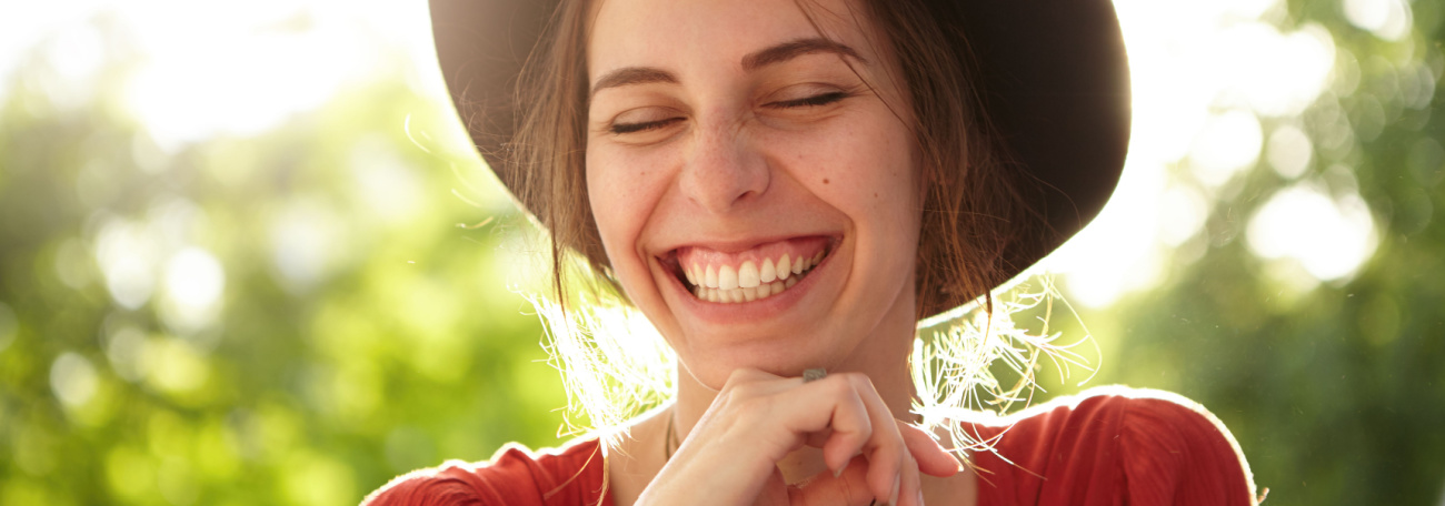 big smile on young woman in nature with a wide brimmed hat and red top