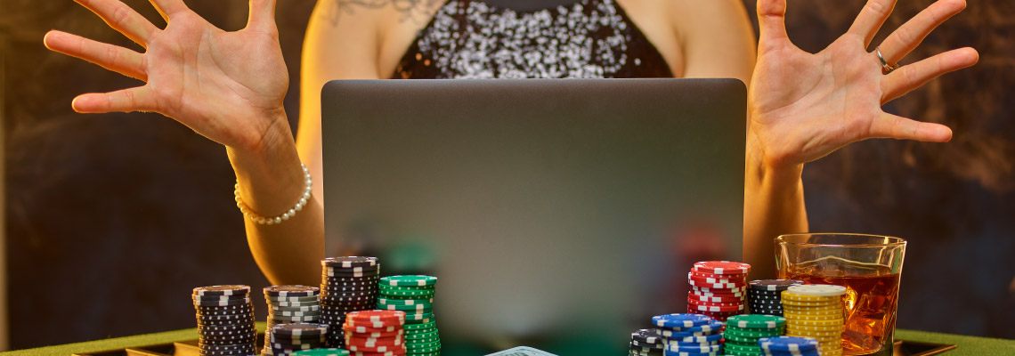 woman playing online casino games on her laptop sitting at a poker table with cards and chips all around.