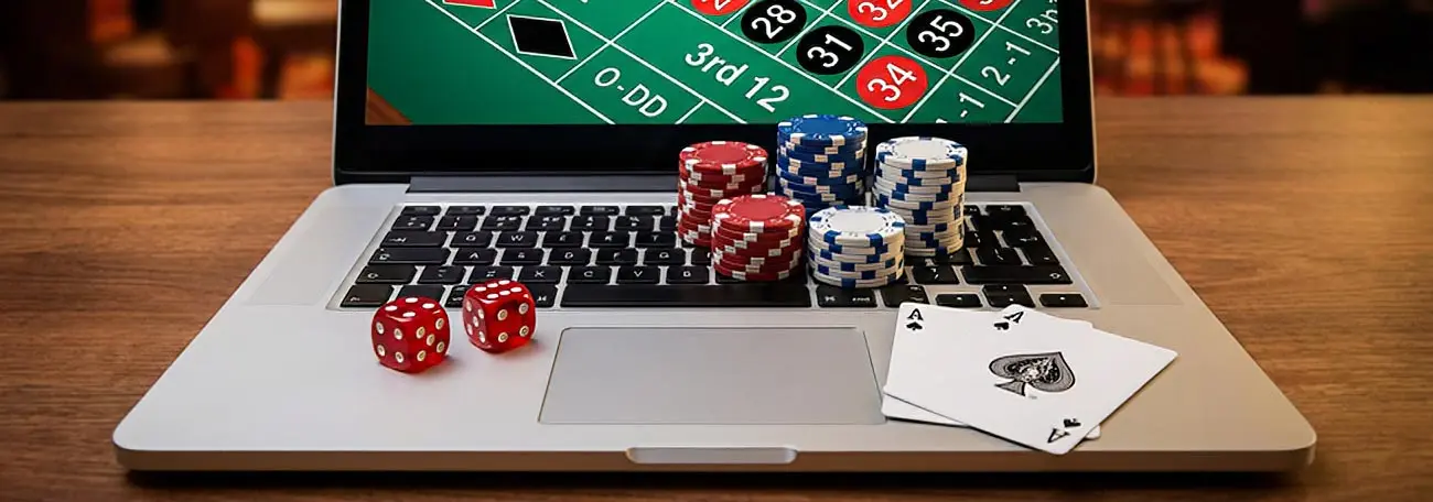 casino gaming items on a laptop including chips, dice, two aces plus a visual of a corner of a roulette table