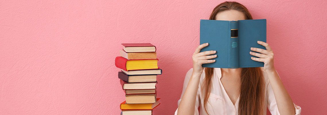 a young woman sitting on the floor reading a book with a stack of 22 books next to her