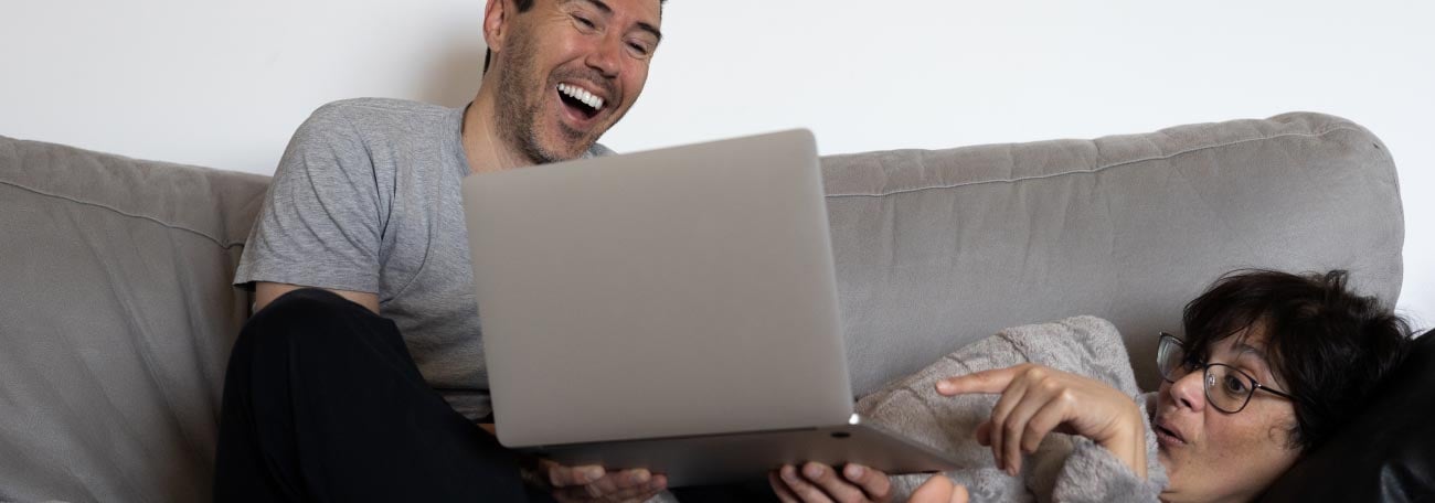 a happy young couple lounging all over each other on the sofa playing on their laptop computer