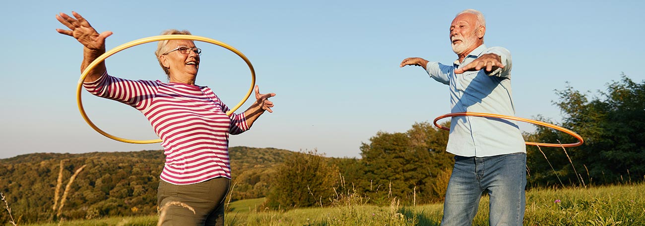 happy older couple playing with hula hoops outdoors in an open field