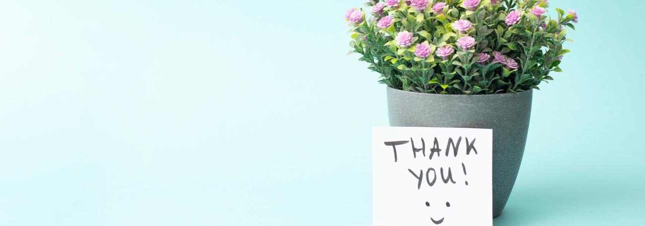 a small planter with pretty pink flowers in it and a thank you note resting on the planter with a smiley face on the note