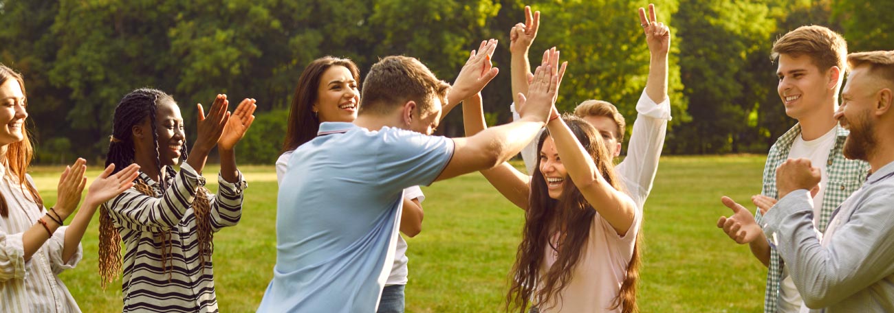 Friends having a great time playing a game outdoors. A man and a woman are giving each other a high five and the others cheer.