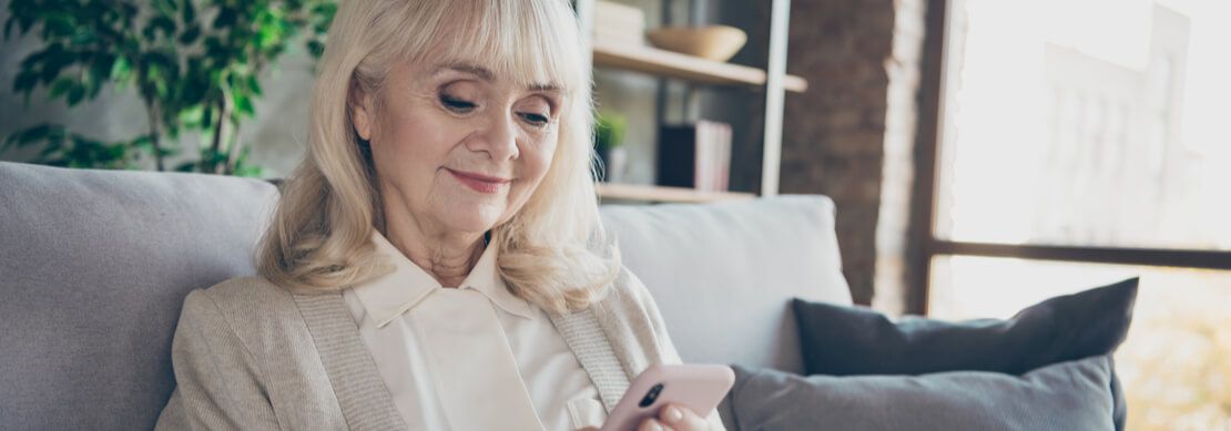 an older lady sitting on her sofa playing on her mobile phone