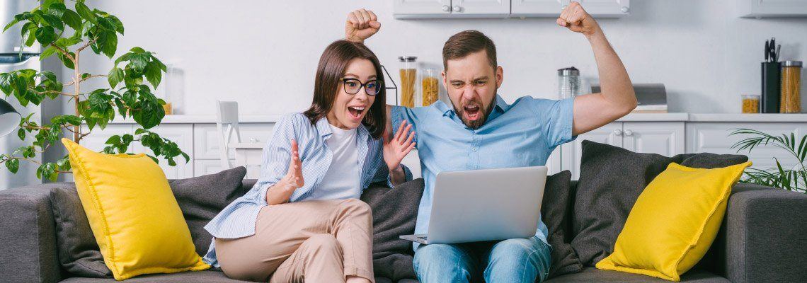 a young couple enjoying online casino gaming while on their sofa. They have just won so they are expressing the joy of winning.