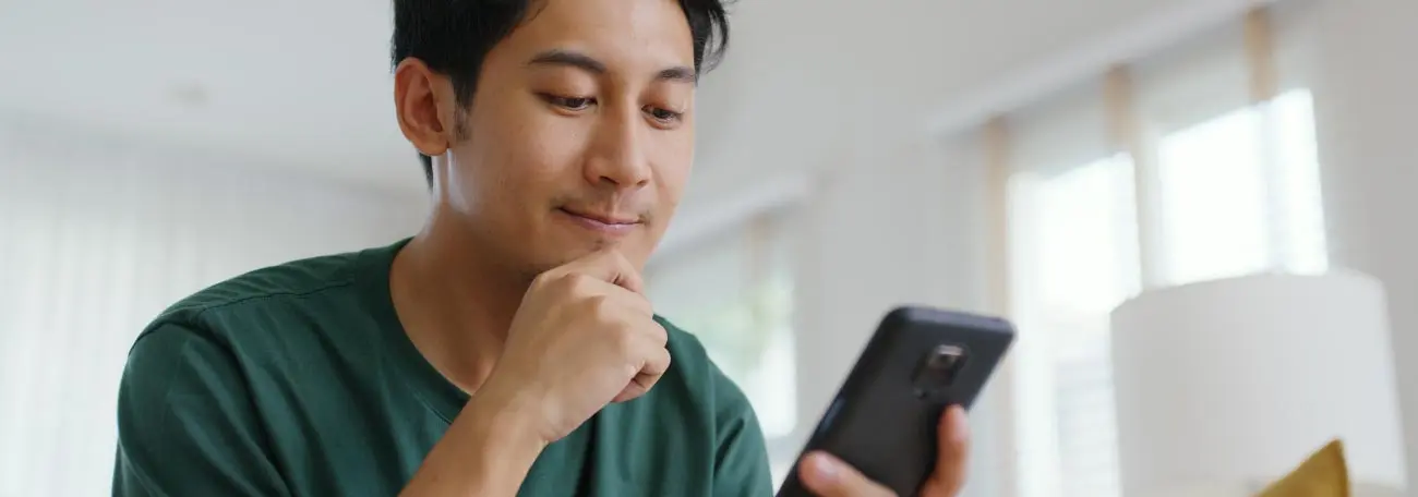 Young Asian man at his smartphone wondering how to get started playing at Jackpot Capital online casino.