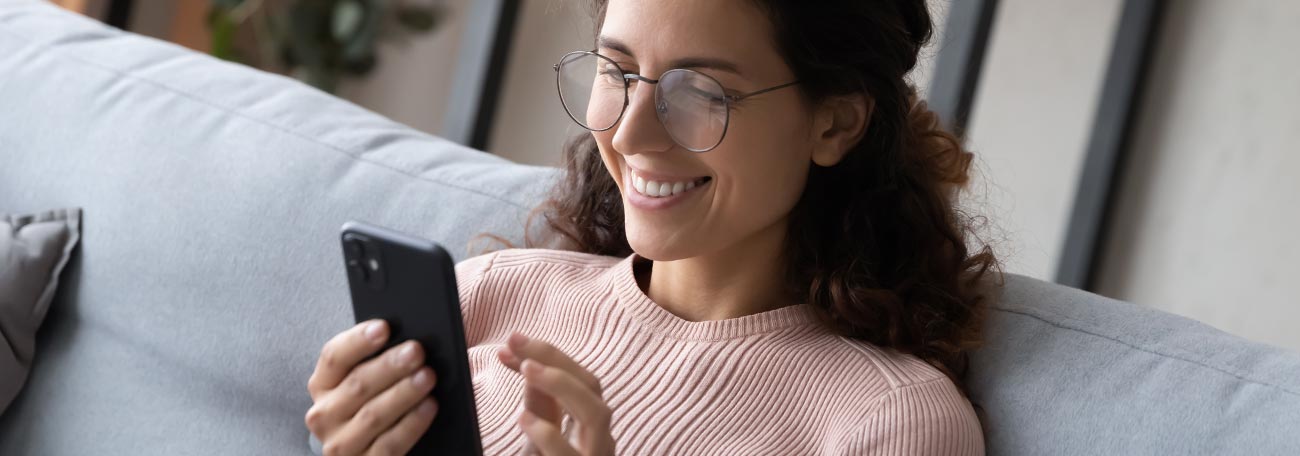 an attractive young woman enjoying gaming on her mobile phone while relaxing on her sofa