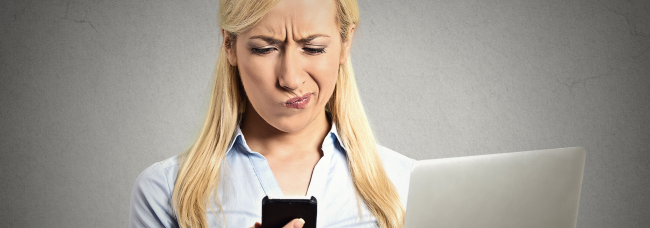 An image of a woman in thought holding a laptop and smartphone against a grey background