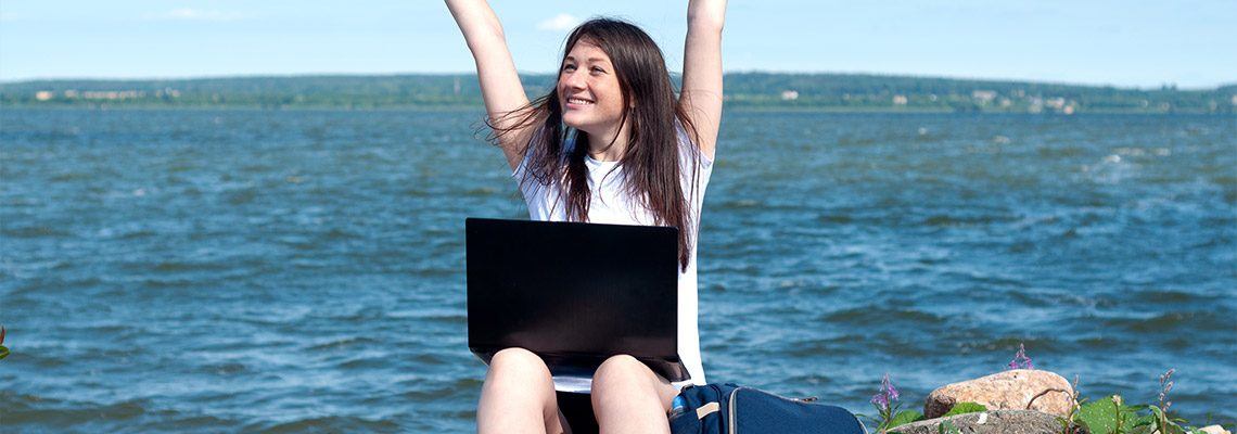 a happy young woman at the ocean playing online casino games on her laptop computer while she enjoys the ocean setting