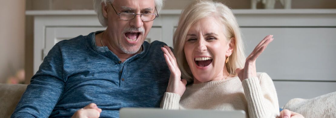 a middle aged couple sitting on the sofa happy because they've just won on a slot game on their laptop