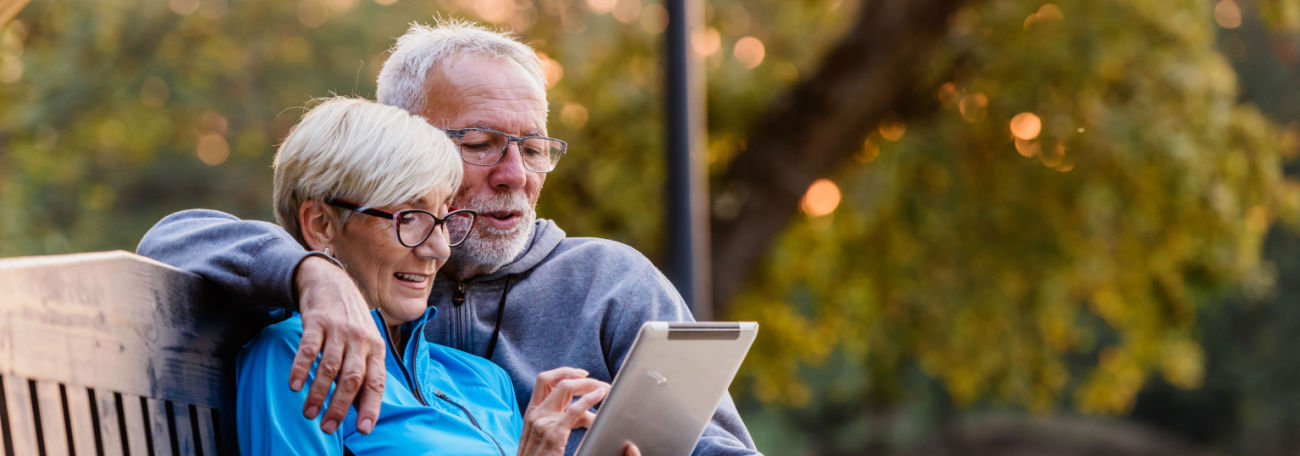 older couple enjoying a moment on a tablet sitting on an outdoor bench for two in the country