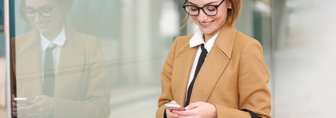 an attractive, smiling young professional woman with large glasses and a tie playing a few spins on her mobile device.
