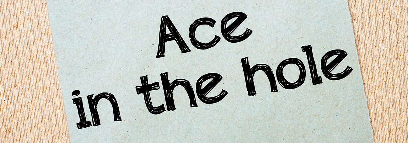 ace in the hole on a small paper pinned to a board. The letters are dark against a light background set at a 45 degree angle