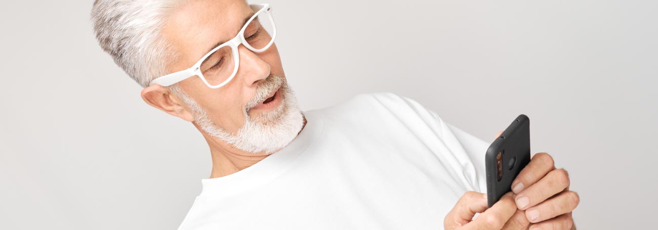 older man with white hair and short white beard looking at his mobile device as he plays online casino games