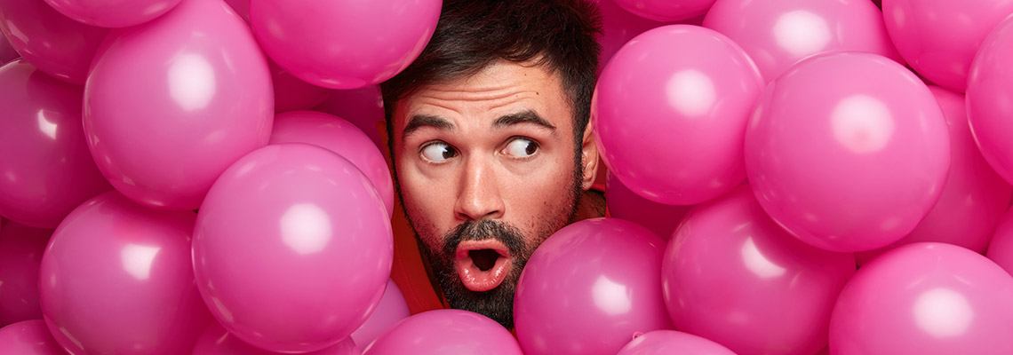 a young man with a short cropped beard immersed in a sea of pink balloons following the tip of letting ourselves be entertained