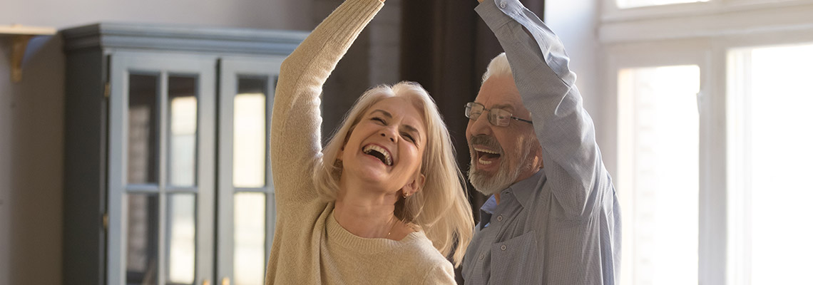 an older couple enjoying dancing together in their living room.  the man is twirling the woman around.