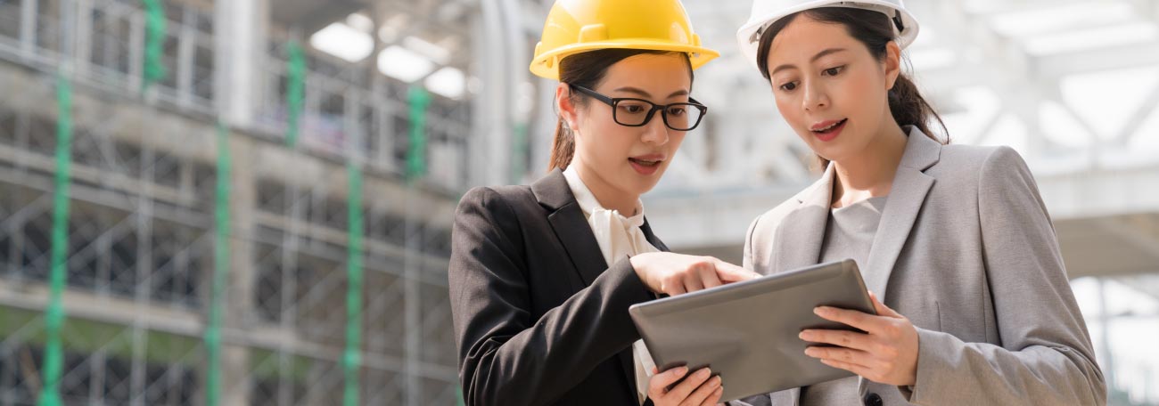 two business women wearing businee suits and hard hats on site going over the details of a building project