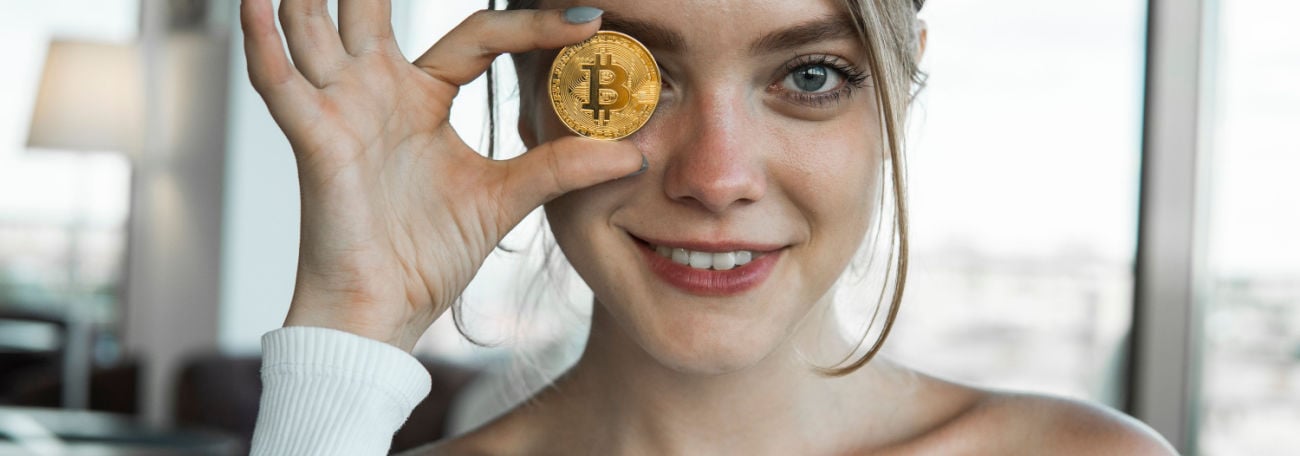 attractive, smiling gen Z woman holding a bitcoin to the camera