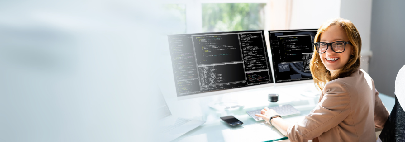 a smiling and attractive young woman with large glasses developing software working at two screens