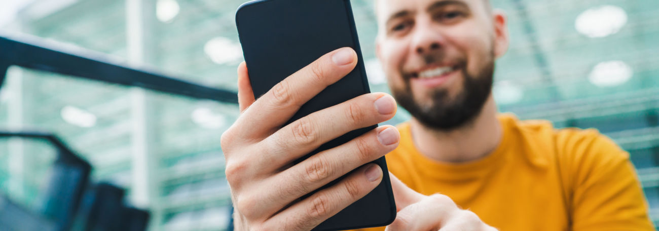 a young man with a broad smile and a trim beard placing a bet on his smartphone while he attends a sporting event