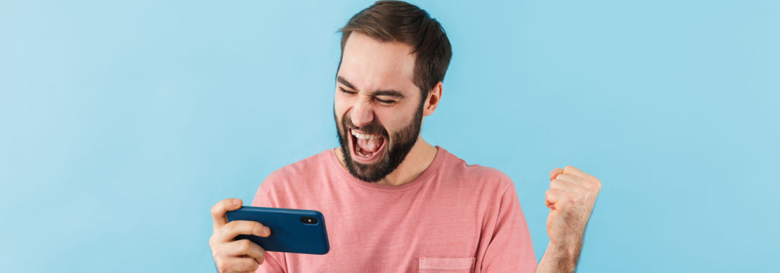 young man in a pink tshirt celebrating after winning playing casino games on his mobile device